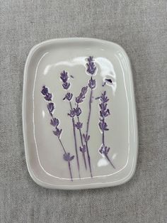 a white plate with purple flowers on the side and grey linen in the back ground