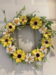 a wreath with yellow and white flowers hanging on a door