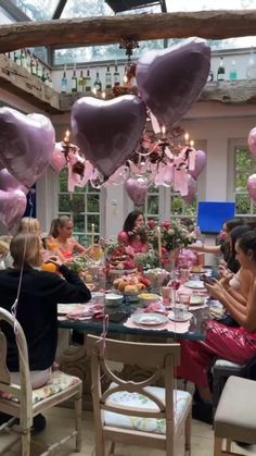 a group of people sitting around a table with heart shaped balloons hanging from the ceiling