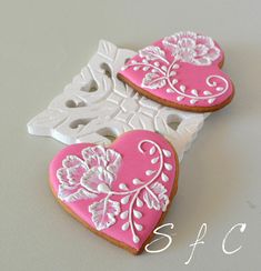 two decorated heart shaped cookies sitting on top of a white box with pink frosting