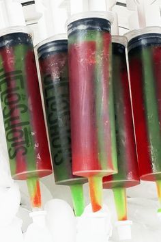 four different colored drinks in plastic cups hanging from the ceiling with white lights behind them