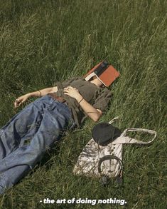 a person laying in the grass with a book and hat on their head next to a pair of scissors