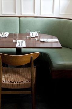 a corner booth with green booths and wooden tables set up for two people to eat