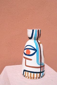 a ceramic vase sitting on top of a white table next to a brown and pink wall