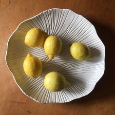 four lemons on a white plate sitting on a wooden table