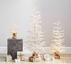 three small white christmas trees sitting next to each other on top of a wooden floor