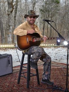 a man sitting on top of a stool holding a guitar in front of a microphone