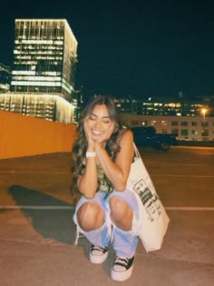 a woman sitting on the ground with her legs crossed and holding a bag in front of her