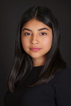 a woman with long black hair wearing a black sweater and posing for a photo in front of a dark background