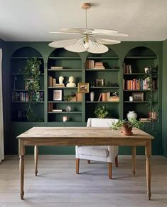 a dining room with green walls and wooden table surrounded by bookshelves filled with plants