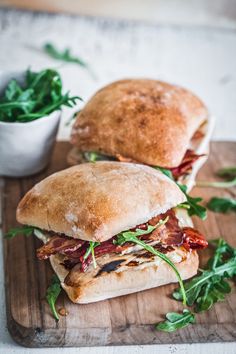 two sandwiches sitting on top of a wooden cutting board next to a bowl of greens