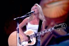 a woman singing into a microphone while holding a guitar