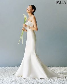 a woman in a white wedding dress holding a bouquet of flowers and looking up at the sky