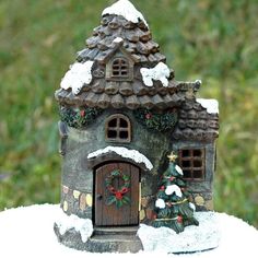 a small house with snow on the roof and christmas decorations around it, sitting in front of grass