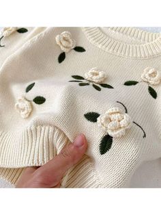 a hand is holding onto a sweater with flowers on the front and back of it