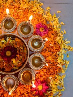 an arrangement of candles and flowers in a bowl on the ground with petals around it