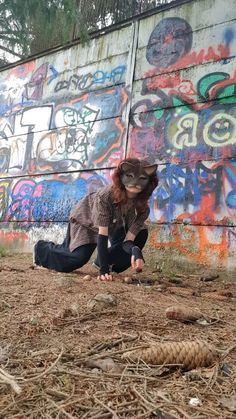 a woman kneeling down in front of a wall with graffiti on it