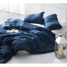 an unmade bed with blue sheets and pillows on the floor next to a lantern