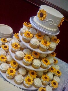 a wedding cake and cupcakes are arranged on a table with sunflowers