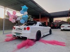 a white car with pink and blue balloons on top