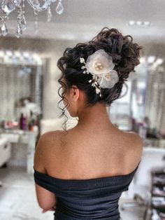 a woman in a black dress with flowers in her hair looking into the distance while standing next to a chandelier