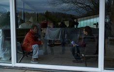 a man sitting on a chair next to a little boy in front of a window