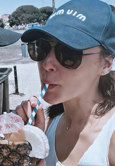 a woman in sunglasses and a hat drinking from a straw