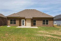 a brick house sitting on top of a lush green field next to two garages