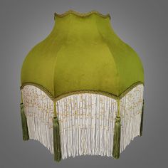 a green lamp shade with white fringes and beads hanging from it's sides