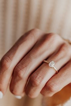 a woman's hand wearing a gold ring with an oval shaped diamond on it