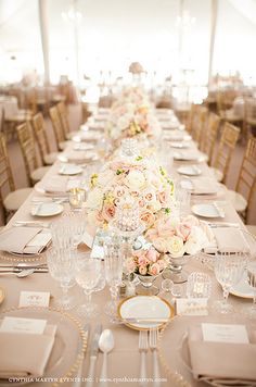 a long table is set with white and pink flowers, silverware and place settings