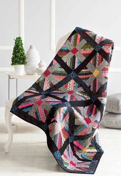 a black and pink quilt sitting on top of a white chair next to a potted plant