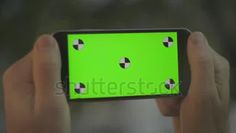 a person holding up a cell phone with green screen and four black dots on it