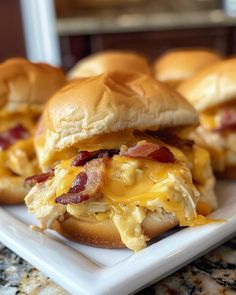 three sandwiches with cheese and bacon on them sitting on a square white plate next to another sandwich