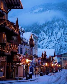 the town is decorated for christmas with lights and decorations on it's buildings, along with snow covered mountains in the background