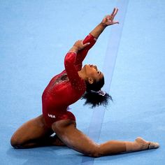 a woman in a red leotard doing a splitstand on the floor