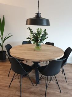 a round wooden table surrounded by black chairs and a potted plant in the center