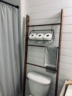 a white toilet sitting next to a wooden ladder in a bathroom under a shower curtain