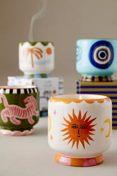 three colorful cups sitting next to each other on top of a white table with a candle in the middle