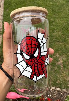 a person holding up a glass jar with a spiderman painted on the front and side