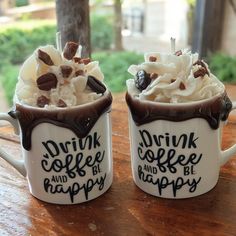 two coffee mugs with whipped cream and chocolate toppings on them sitting on a wooden table