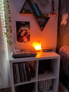 a small white shelf with some records on it and a candle in front of it