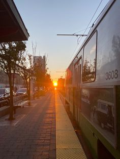 the sun is setting behind a train on the tracks in front of some parked cars