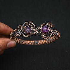 a close up of a person holding a piece of metal with purple stones on it