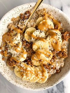 a white bowl filled with rice and bananas covered in caramel sauce on top of a marble counter