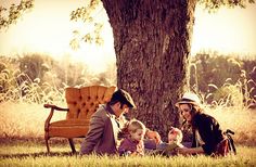 a family sitting under a tree in the grass with an adult and two small children