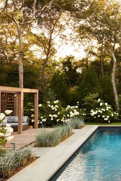 a pool surrounded by white flowers and greenery next to a wooden pergoline