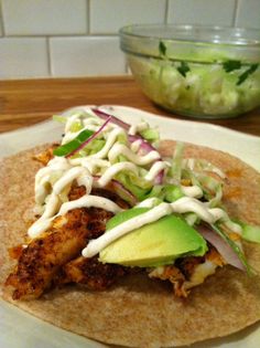 a taco with chicken, lettuce and sauce on it next to a bowl of coleslaw