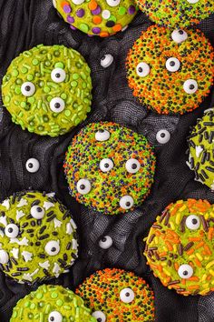 decorated cookies with eyes and sprinkles are on a black cloth covered table