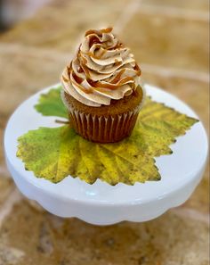 a cupcake sitting on top of a plate with leaves around it and frosting